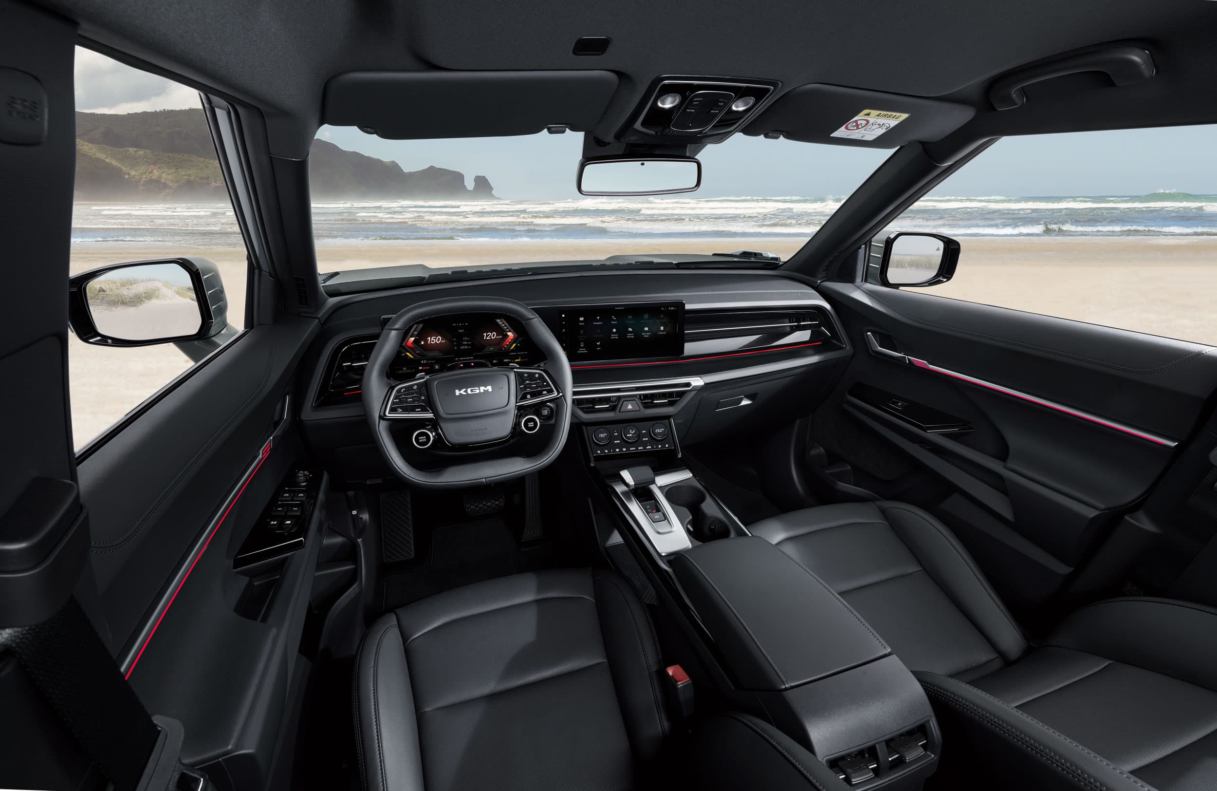 Modern KGM Torres interior with a black dashboard, steering wheel, and seats. Ocean and mountains visible through the windshield.