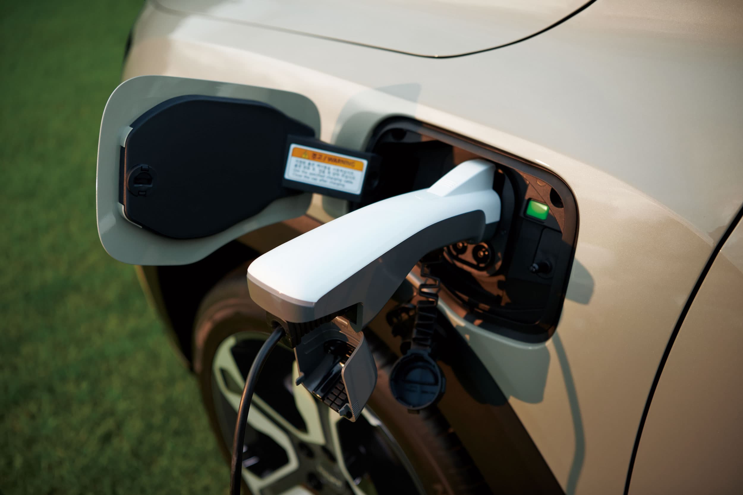 KGM Torres EVX being charged with a charger plugged into the side port, parked on grass.