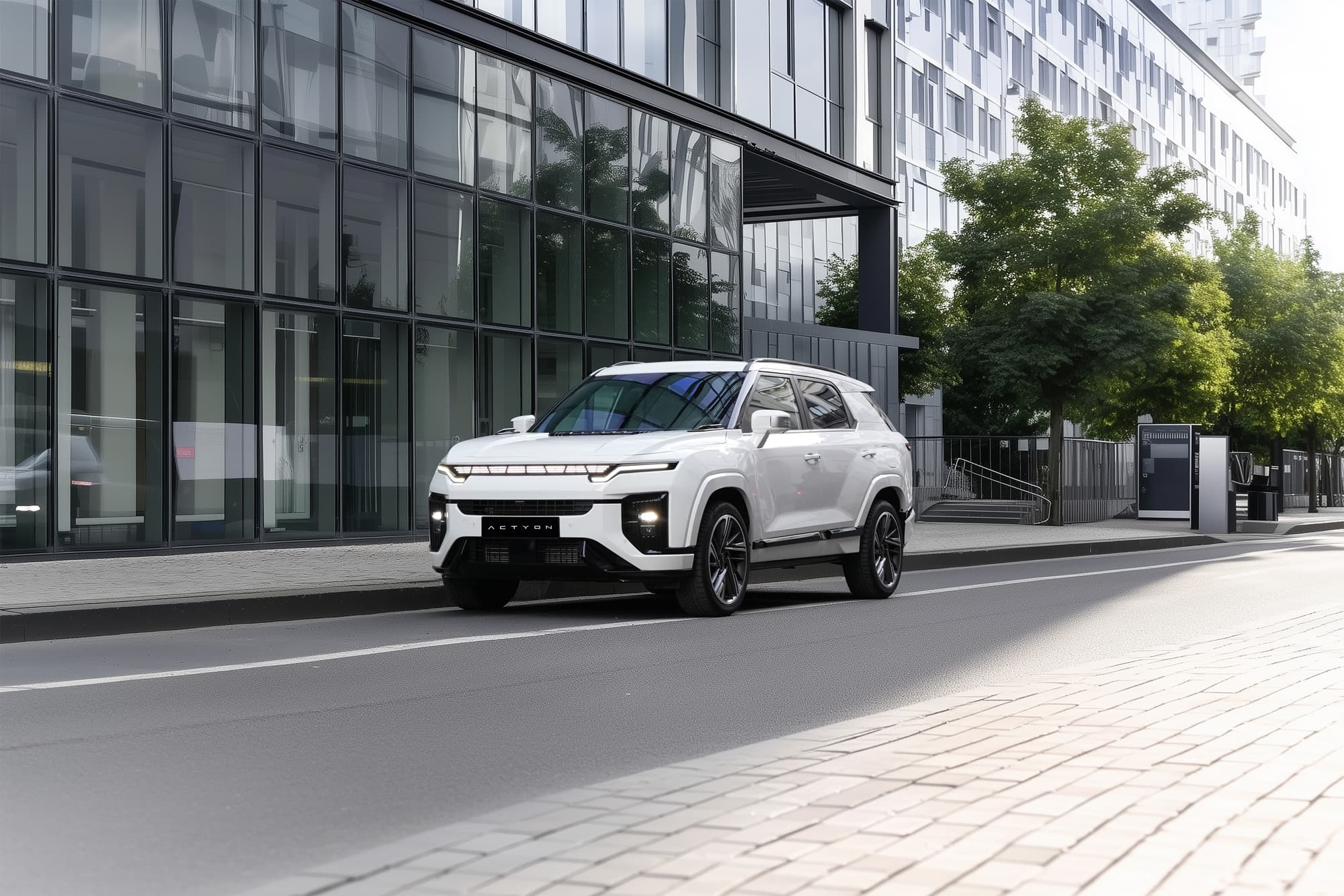 White KGM Actyon Hybrid parked on a city street in front of a modern glass office building with trees and a paved sidewalk.